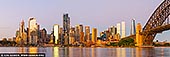 australia stock photography | Sydney City at Dawn, Sydney, New South Wales (NSW), Australia, Image ID AU-SYDNEY-0034. The photo captures a stunning view of Circular Quay and Sydney City at sunrise, taken from across the harbor. The entire cityscape is bathed in a warm, golden light, which highlights the modern skyline's diverse mix of skyscrapers and historic buildings. The sunlight reflects off the glass facades, casting a soft, amber glow that enhances the architectural details of each structure. Circular Quay, bustling with ferries and boats, is nestled along the water's edge, its iconic wharves shimmering under the sunrise's brilliance. The calm harbor waters mirror the glowing city, creating a breathtaking display of light and color. In the background, the fading sky is a blend of deep oranges, pinks, and purples, adding a sense of drama and serenity to the scene.