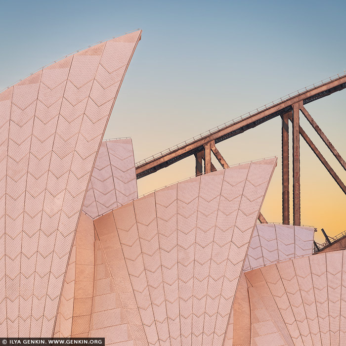 australia stock photography | Sydney Opera House Sails at Dawn, Sydney, NSW, Australia. An intimate close-up of the Sydney Opera House sails, their iconic, curving white tiles bathed in the soft golden and pink hues of sunrise. The intricate texture of the sails is illuminated, showcasing their delicate yet striking architectural detail. In the background, a portion of the Harbour Bridge arches gracefully into the frame, its steel structure silhouetted against the pastel-coloured sky. The interplay of light and shadow captures the tranquil beauty of this early morning moment in Sydney.