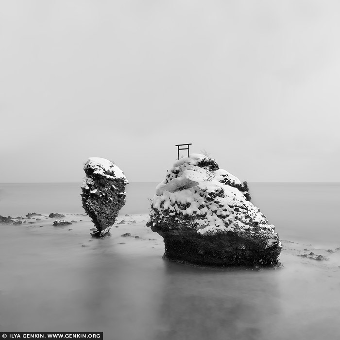 portfolio stock photography | Ebisu Iwa. Study 1, Yoichi, Hokkaido, Japan. A long exposure black-and-white photograph captures the serene beauty of Ebisu Iwa and Daikoku Rock off the rugged coast of Yoichi, Hokkaido. The stark contrast between the dark, jagged rock formations and the smooth, misty surface of the sea creates a hauntingly tranquil scene. The extended exposure blurs the motion of the ocean, turning the waves into a silky, ethereal fog that wraps around the ancient rocks like a soft veil. Above, the sky is rendered in subtle grey tones, adding depth and mood to the composition. The monochrome palette emphasises the textures of the weathered stone and the gentle movement of the water, evoking a timeless, almost otherworldly atmosphere. The scene feels isolated yet majestic, a quiet testament to natureâ€™s enduring strength and beauty.