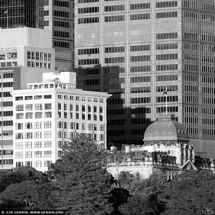 portfolio stock photography | The Astor and Chief Secretary's Building, Sydney, NSW, Australia. In this black-and-white photograph, the heritage-listed Chief Secretary's Building, originally and still commonly known as the Colonial Secretary's Building, and The Astor, one of Sydney's most distinguished residential buildings, create a captivating contrast against the modern high-rises of Sydney's evolving skyline. The Chief Secretary's Building stands as a masterpiece of Victorian Free Classical architecture, its richly ornamented facade adorned with detailed pilasters, archways, and a clock tower crowned with a delicate dome. The intricate stonework and classical proportions exude a dignified charm, evoking Sydney's colonial history. Nearby, The Astor â€” a distinguished residential building in the Interwar Free Classical style â€” rises with its solid brick and sandstone facade, boasting tall, arched windows and restrained, elegant detailing that emphasise its enduring sophistication. These historic structures are juxtaposed against sleek, contemporary skyscrapers that loom above them, their minimalist glass and steel facades reflecting light in sharp, angular patterns. This striking composition of old and new highlights Sydney's layered architectural identity, where heritage buildings like the Chief Secretary's Building and The Astor retain their presence and dignity amidst the city's continual growth and transformation. The photo captures an architectural dialogue between the historic and the modern, reminding viewers of Sydney's respect for both legacy and innovation.