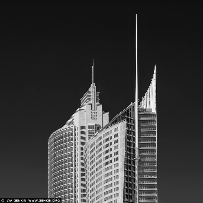 portfolio stock photography | Aurora Place and Chifley Tower, Sydney, NSW, Australia. In this black-and-white photograph, Aurora Place and Chifley Tower rise prominently against Sydney's sky, captured in striking detail. Aurora Place, with its curved, sail-like facade, reflects light in varying shades of grey, giving the building a fluid, almost organic presence against the static background. The glass curtain walls of Aurora Place arc gently, with a delicate texture that contrasts its modern, angular neighbouring structures. Beside it stands Chifley Tower, its sleek, stepped design and clean vertical lines embodying the late 20th-century corporate aesthetic. Chifley's smooth concrete and glass surfaces appear slightly darker, grounding it in a timeless, monolithic elegance. The juxtaposition of the two buildings - the organic flow of Aurora Place and the geometric precision of Chifley Tower - illustrates the contrasting architectural philosophies of Sydney's evolving skyline, blending bold modernism with subtle gestures of nature-inspired design.